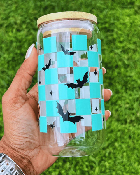 Clear glass can-style cup featuring a playful ghost and a turquoise checkered pattern with bats, complete with a reusable straw—perfect for spooky season.