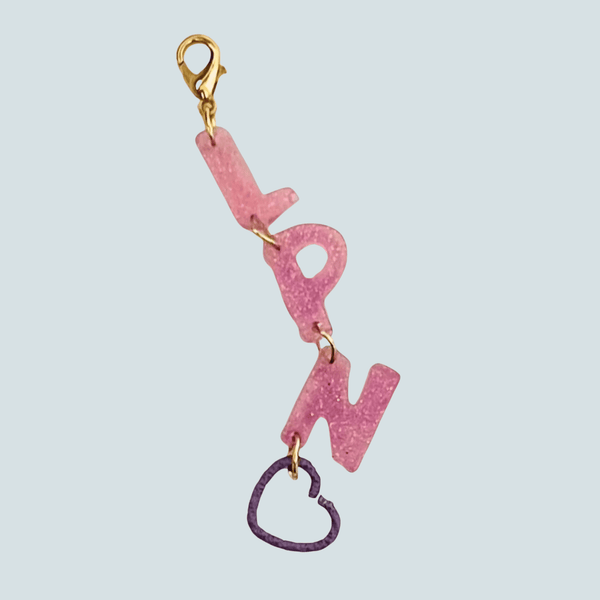 A pink glitter resin badge reel charm showcasing the acronym 'LPN' for Licensed Practical Nurse, accented with a gold clasp and a delicate gold heart charm—ideal for adding sparkle to a nurse's uniform.
