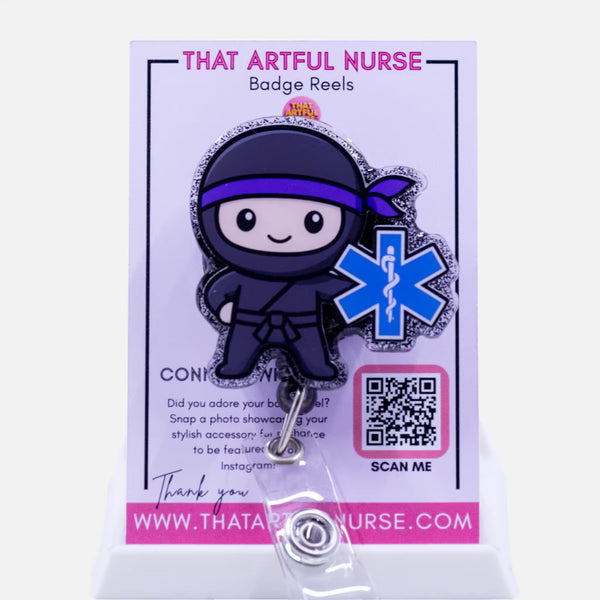 EMS-themed badge reel featuring a cute ninja character with a blue Star of Life symbol and glitter outline, displayed on That Artful Nurse packaging.