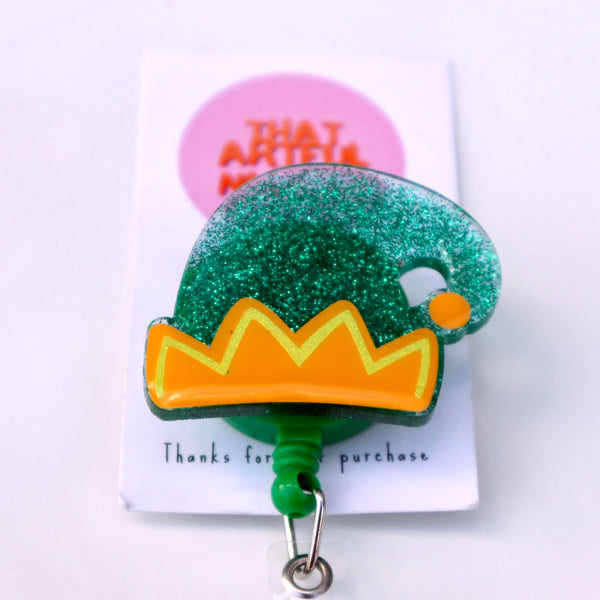 Green acrylic elf hat badge reel with glitter finish and yellow trim detail.