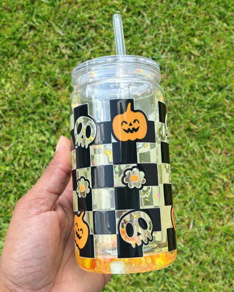16oz Halloween-themed snow globe tumbler with black-and-white checkered pattern, pumpkins, skulls, flowers, and floating glitter.