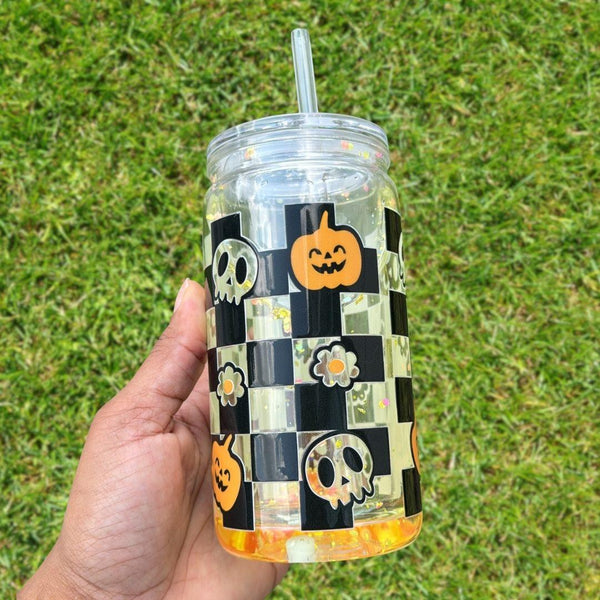 16oz Halloween-themed snow globe tumbler with black-and-white checkered pattern, pumpkins, skulls, flowers, and floating glitter.