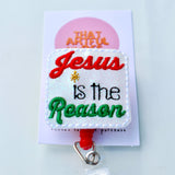 Embroidered badge reel with “Jesus is the Reason” in red, green, and black thread on white fabric.