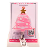 Pink Christmas tree badge reel with glitter snow accents and gold star topper, displayed on That Artful Nurse packaging.