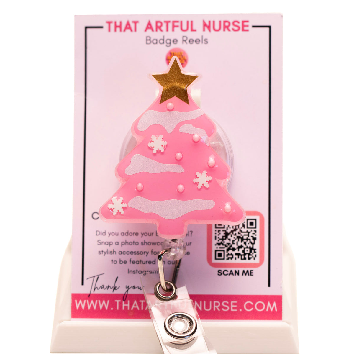 Pink Christmas tree badge reel with glitter snow accents and gold star topper, displayed on That Artful Nurse packaging.
