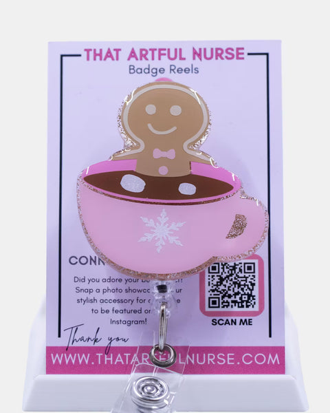 Pink glitter mug badge reel with a smiling gingerbread man in hot cocoa, featuring a white snowflake design and retractable clip.