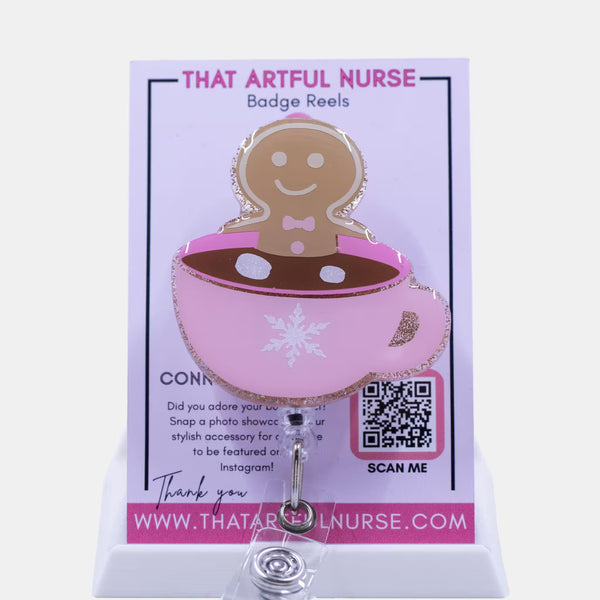 Pink glitter mug badge reel with a smiling gingerbread man in hot cocoa, featuring a white snowflake design and retractable clip.