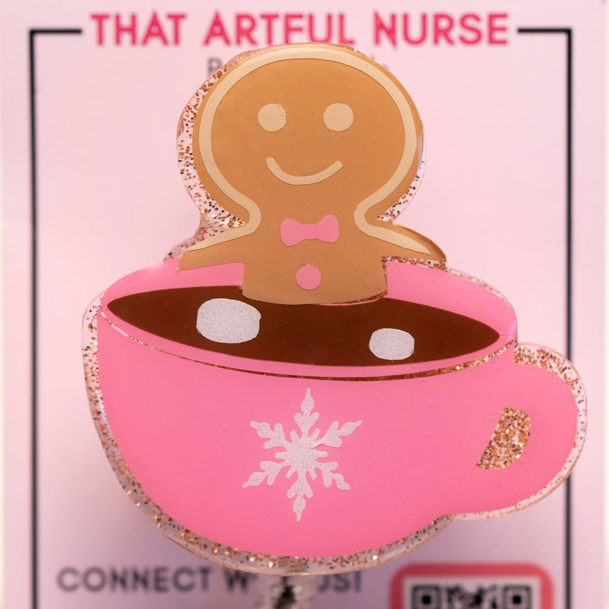 Pink glitter mug badge reel with a smiling gingerbread man in hot cocoa, featuring a white snowflake design and retractable clip.