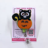 A retractable badge reel featuring a cute black cat sitting on top of a glittery orange pumpkin. 