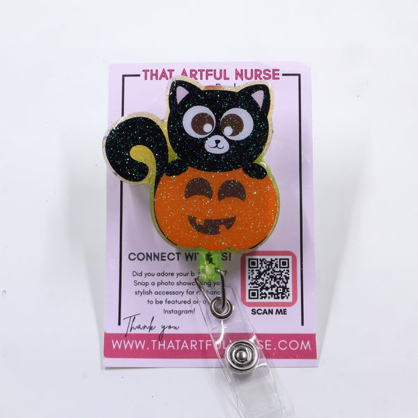 A retractable badge reel featuring a cute black cat sitting on top of a glittery orange pumpkin. 