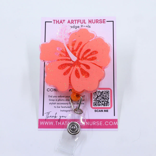 Pink hibiscus flower badge reel from That Artful Nurse displayed on a branded card.