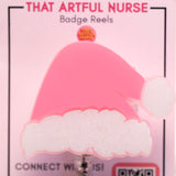 Pink Santa hat badge reel with glittery white trim on a retractable clip, displayed on That Artful Nurse packaging.