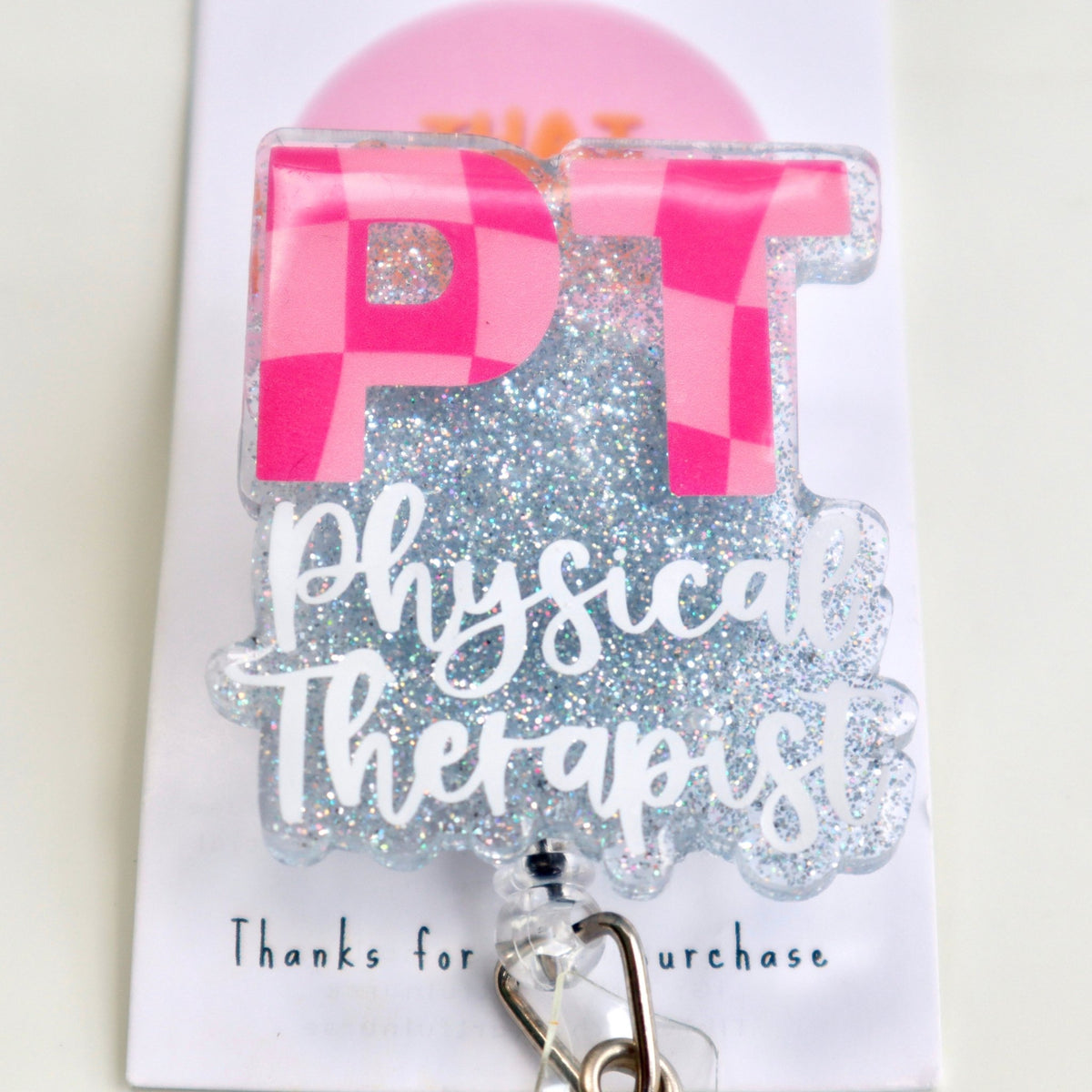 A physical therapist badge reel with two shades of pink colors featuring a checkered design, attached to an ID clip.