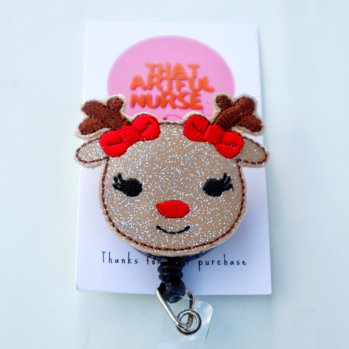 Reindeer-inspired badge reel with glittery face, red nose, lashes, and red bows on antlers.