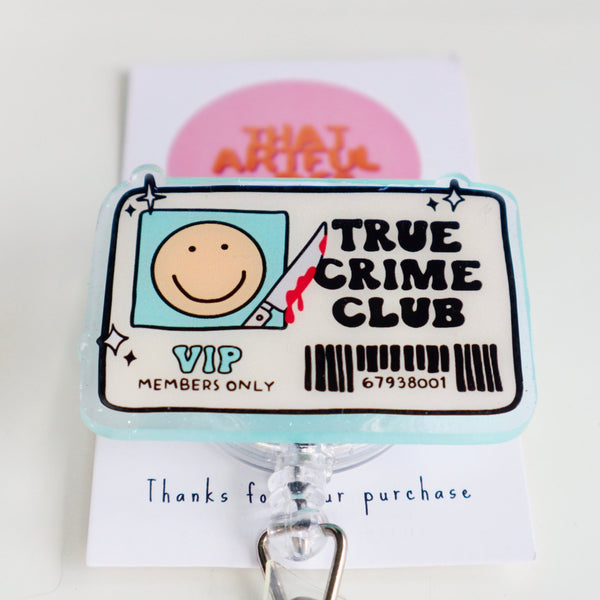 A badge reel with a design that includes a smiley face and the text 'True Crime Club VIP MEMBERS ONLY' with a barcode. The reel is attached to a retractable clip.