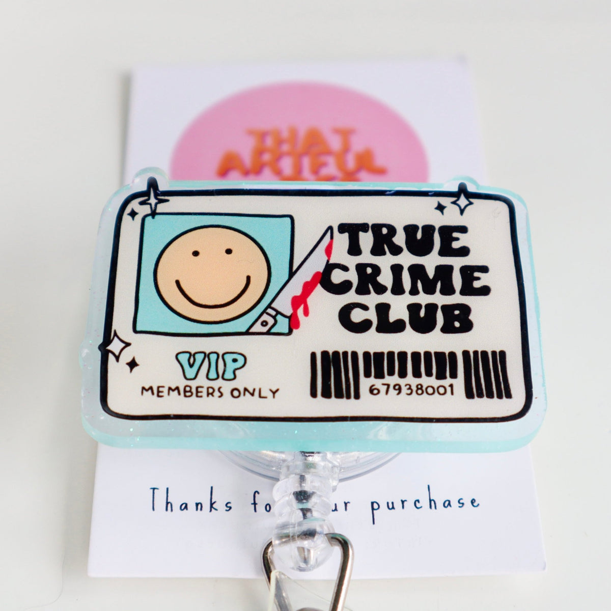 A badge reel with a design that includes a smiley face and the text 'True Crime Club VIP MEMBERS ONLY' with a barcode. The reel is attached to a retractable clip.